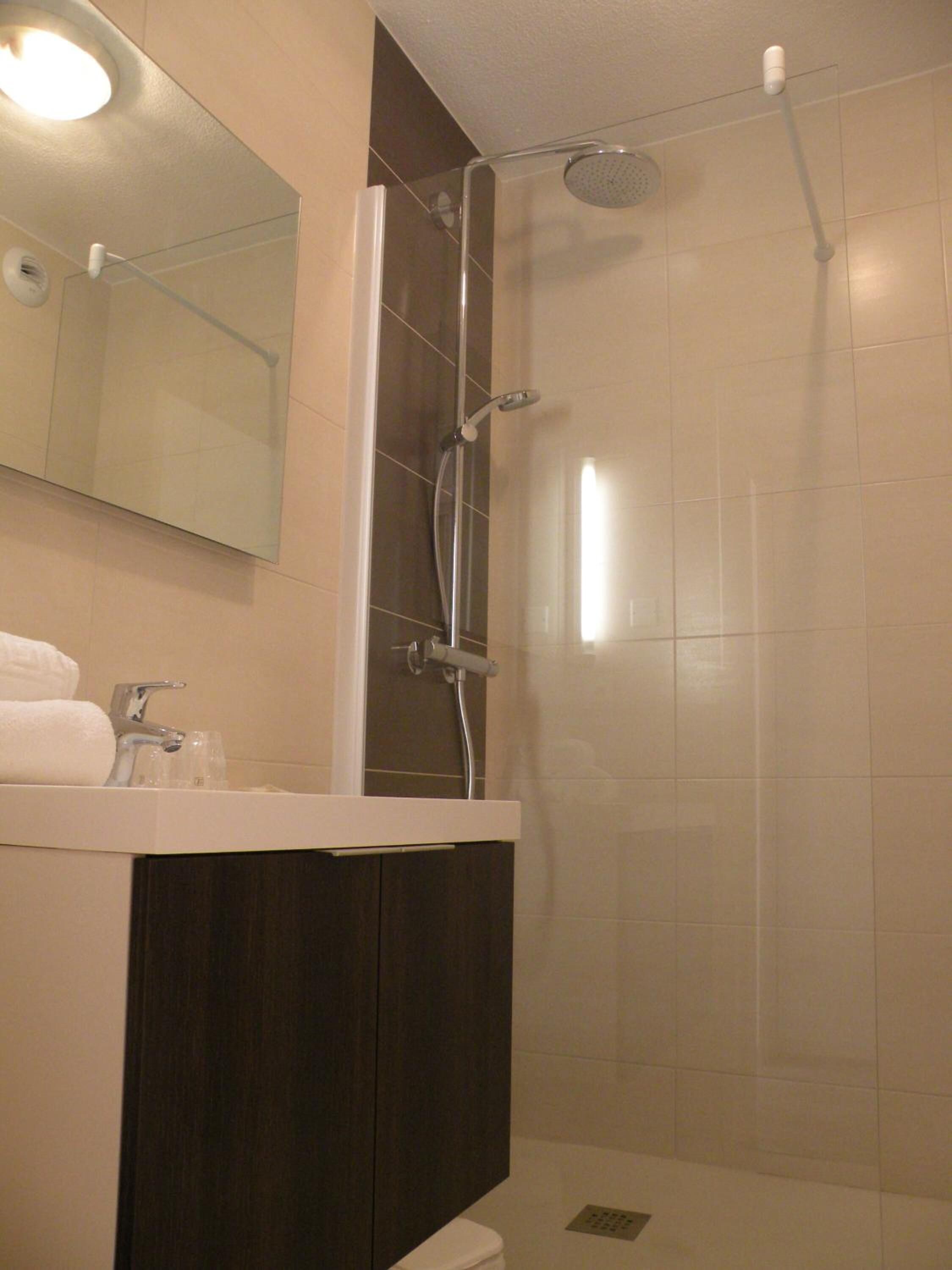 A modern bathroom with a glass-enclosed shower, a white sink with a dark cabinet, and a large mirror above the sink.