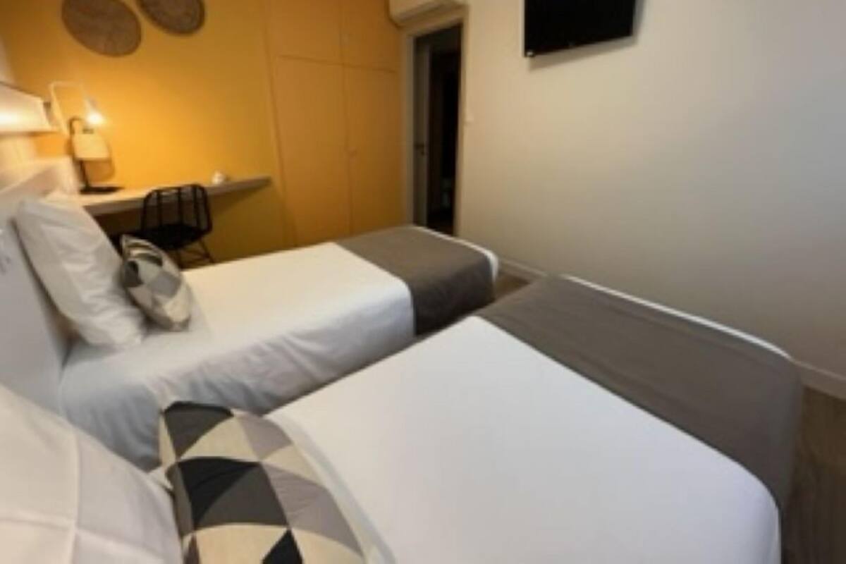 A hotel room with two beds, a desk, a chair, and a flat-screen TV mounted on the wall.