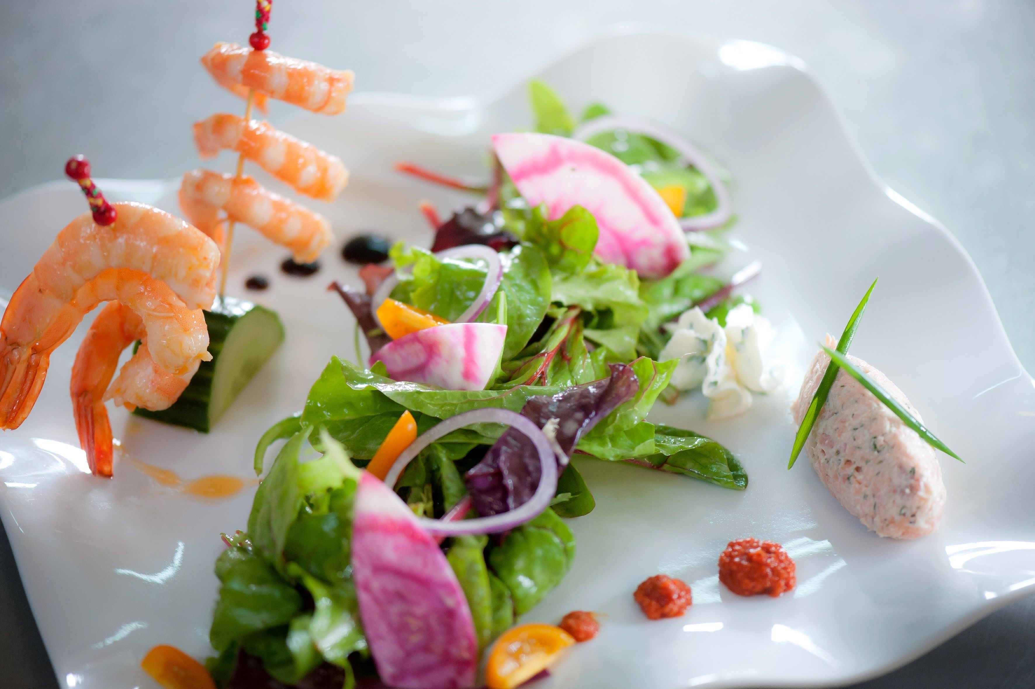 Une assiette avec des brochettes de crevettes, une salade garnie de rondelles de radis et une portion de pâté.