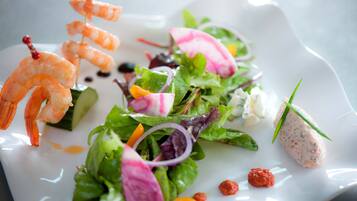 Une assiette avec des brochettes de crevettes, une salade garnie de rondelles de radis et une portion de pâté.
