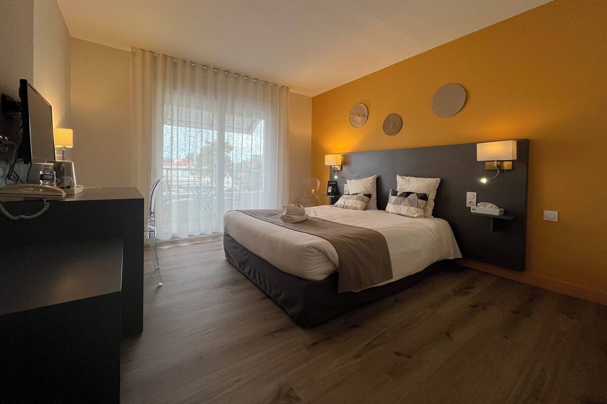 A hotel room with a bed, bedside tables, a desk with a telephone, and a television.