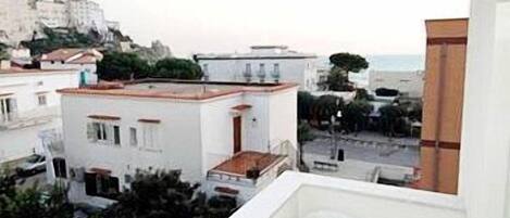 A balcony with a view of a coastal town, white buildings, and a distant mountain.