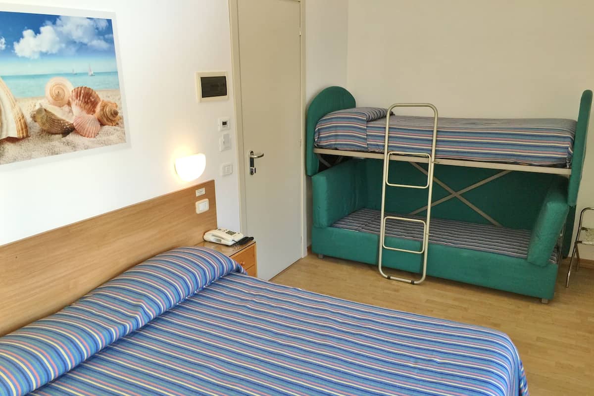 Ein Zimmer mit einem Einzelbett, einem Etagenbett, einem Nachttisch mit Telefon und einer Wandleuchte.