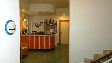 A reception area with a counter, a wicker chair, a lamp, and a wall-mounted sign indicating the reception.