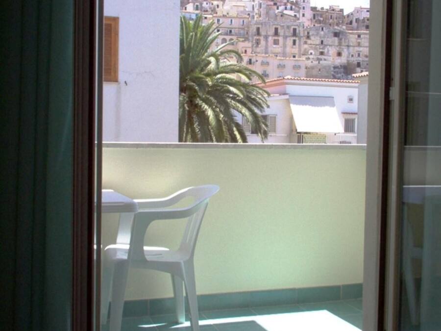 A balcony with a table and chairs, a palm tree, and a view of a densely packed cityscape.