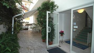 Entrada com porta de vidro, escada e plantas em vasos.