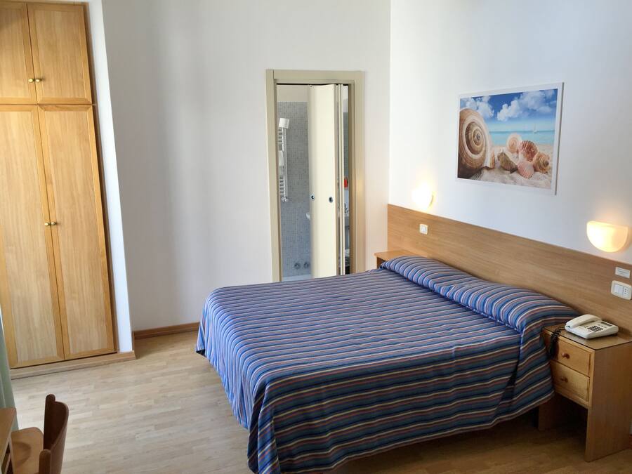 A bedroom with a bed, wooden wardrobe, and a painting of seashells.