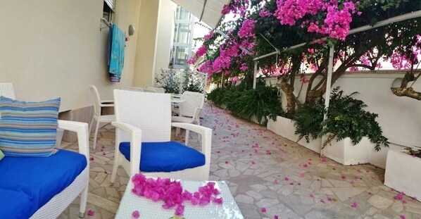 An outdoor seating area with white wicker furniture and blue cushions, surrounded by a stone floor and pink flowers. - Hotel Mayor (Sperlonga)