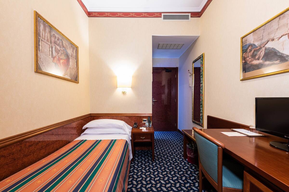 A hotel room with a bed, a desk, a television, and a door leading to another room.