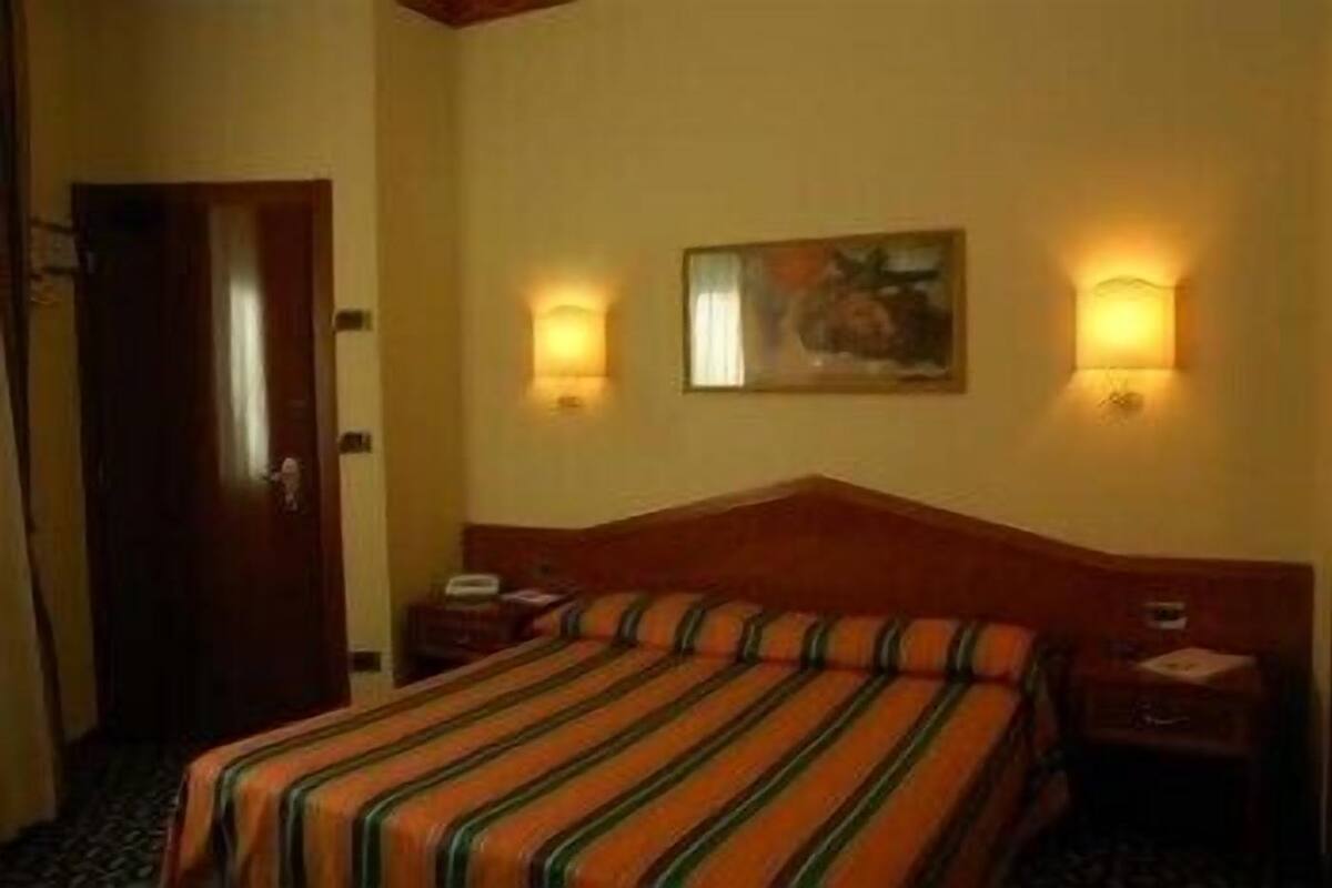 A hotel room with a bed, a nightstand, a lamp, and a painting on the wall.