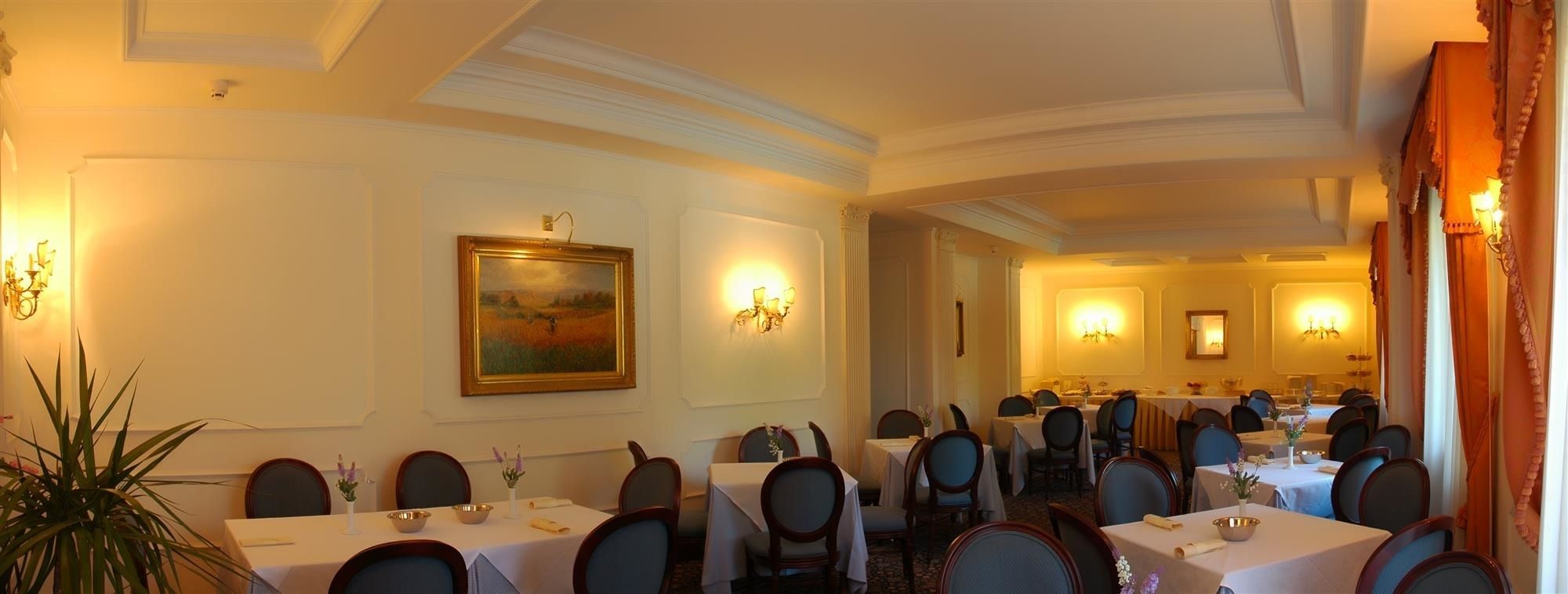 Une salle à manger élégante, avec plusieurs tables et chaises, un tableau au mur et des luminaires fixés au mur.