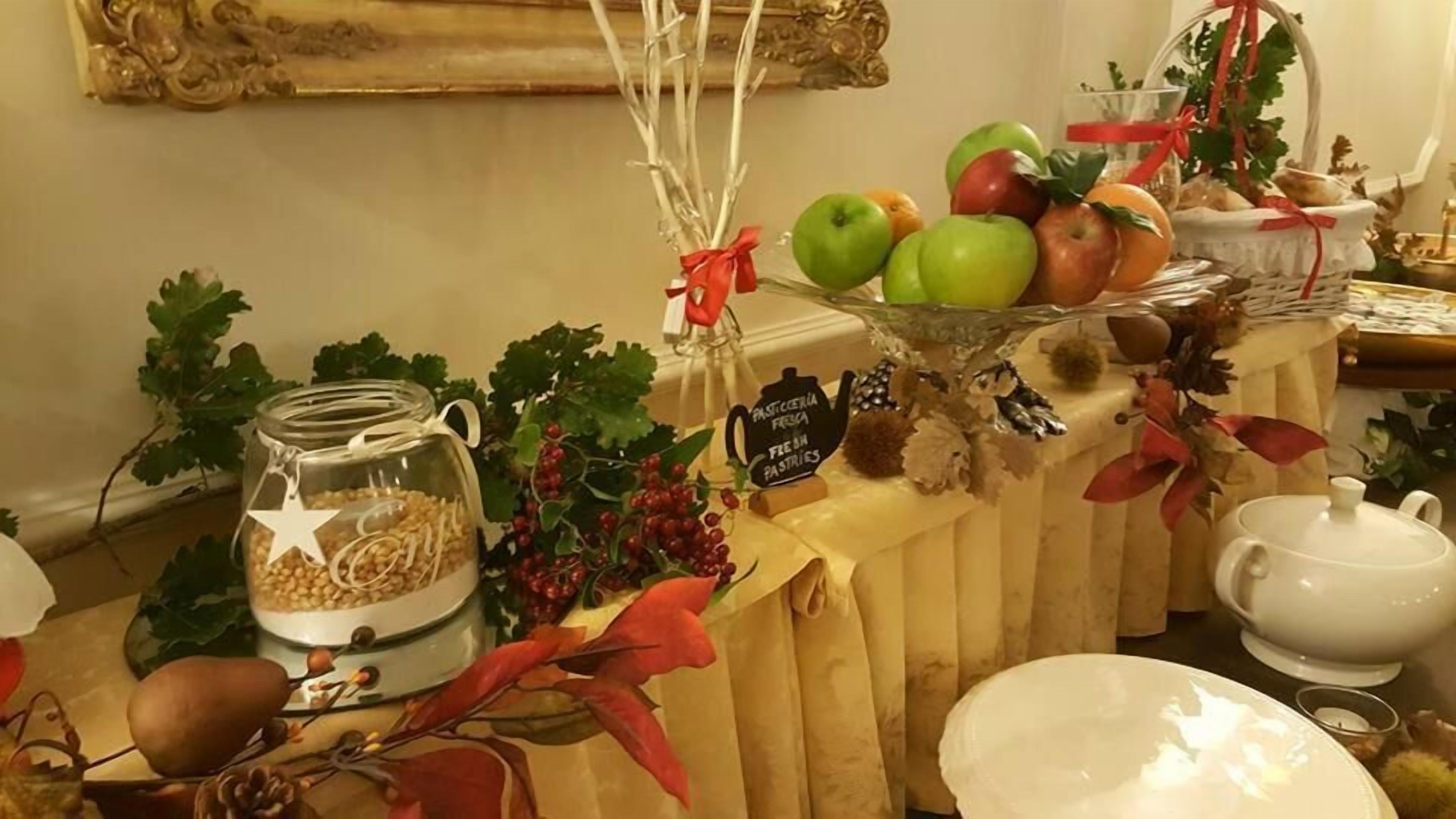 Taula de buffet amb una varietat d'aliments, incloent fruita, un bocal de cereals i un cartell que indica la disponibilitat de pastissos.
