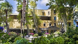 A hotel with a yellow facade, a fountain, and lush greenery. - Hotel Royal (Bolsena)