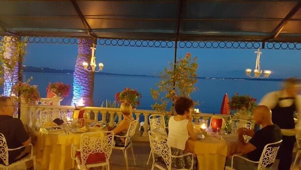 An outdoor dining area with tables and chairs, overlooking a body of water. - Hotel Royal (Bolsena)
