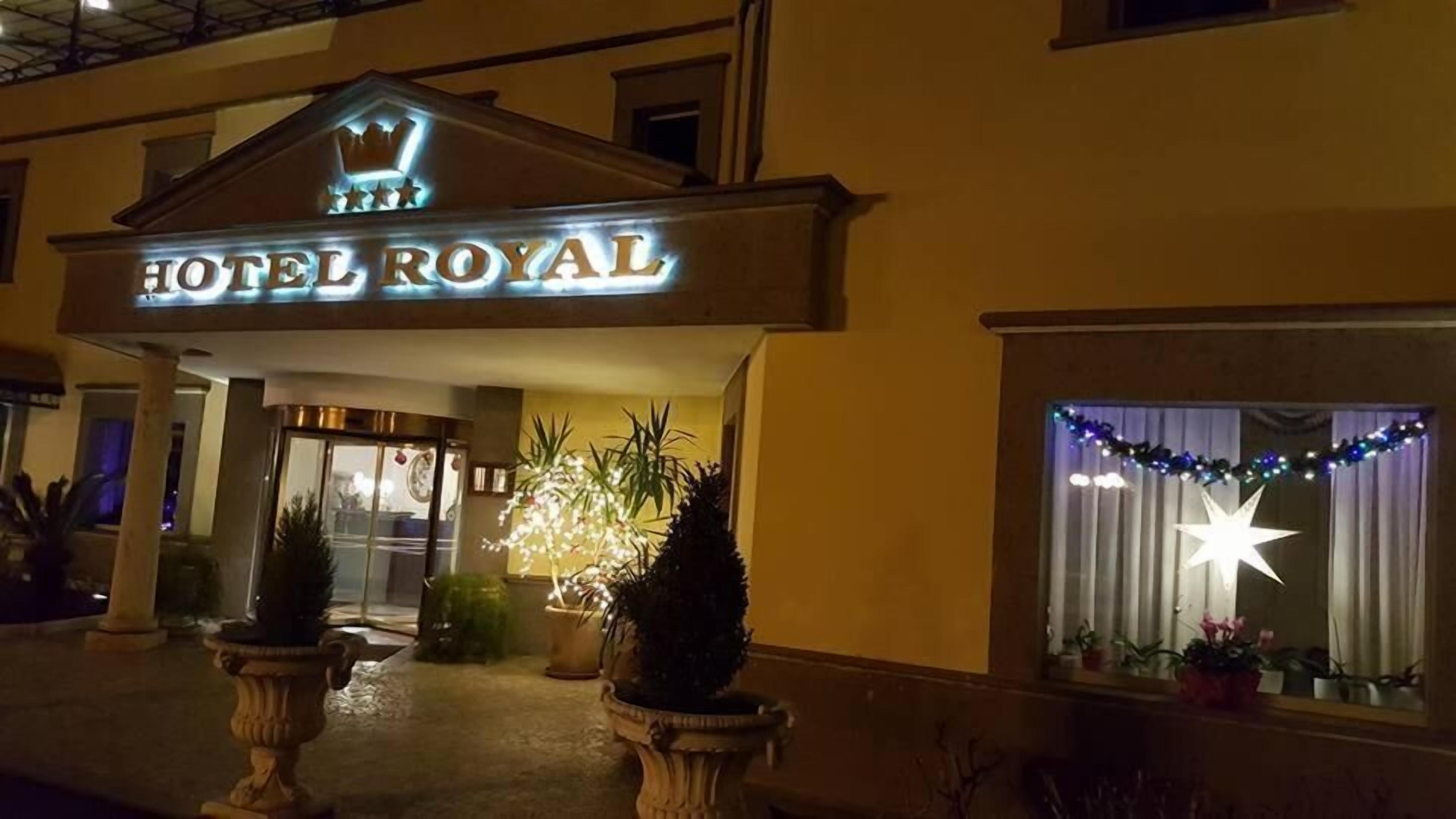 Exterior del Hotel Royal con un llamativo letrero iluminado, una entrada imponente y iluminación decorativa.