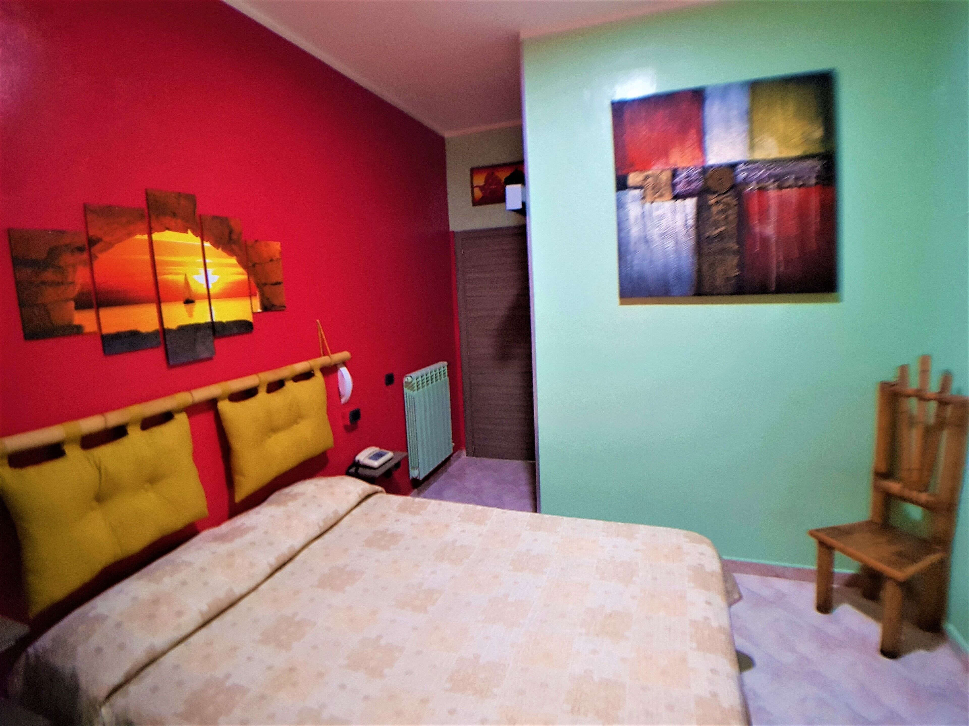 A bedroom with a bed, a radiator, a chair, and a painting on the wall.