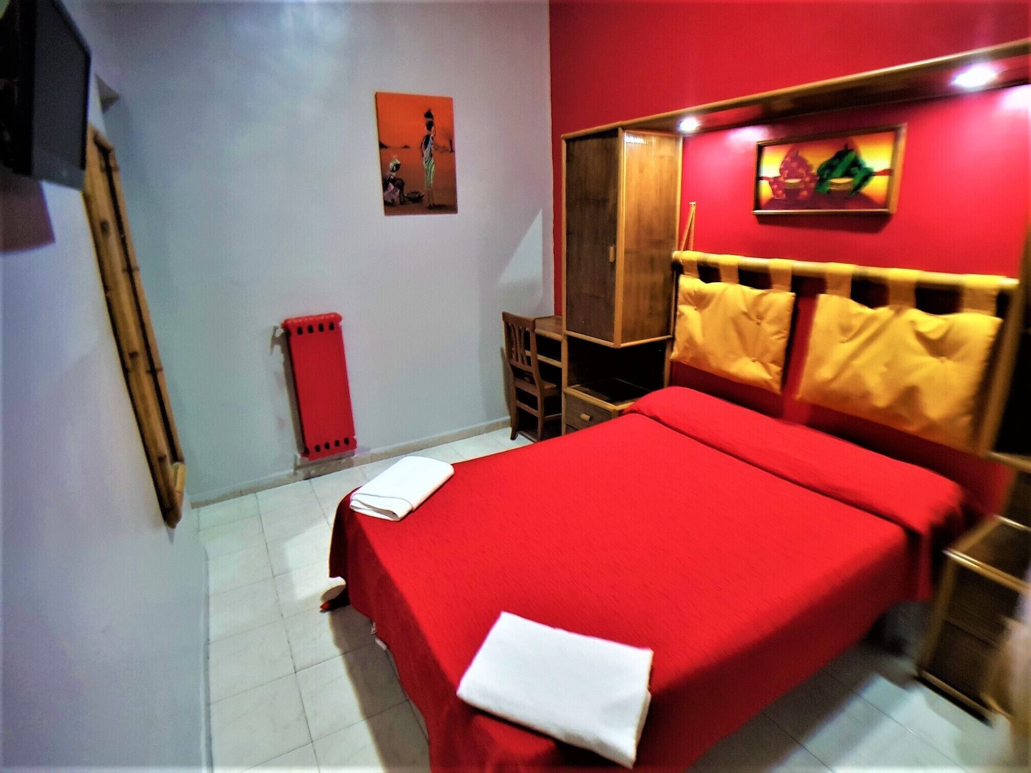 A bedroom with a red bedspread, a wooden headboard, a red radiator, and a small wooden nightstand.