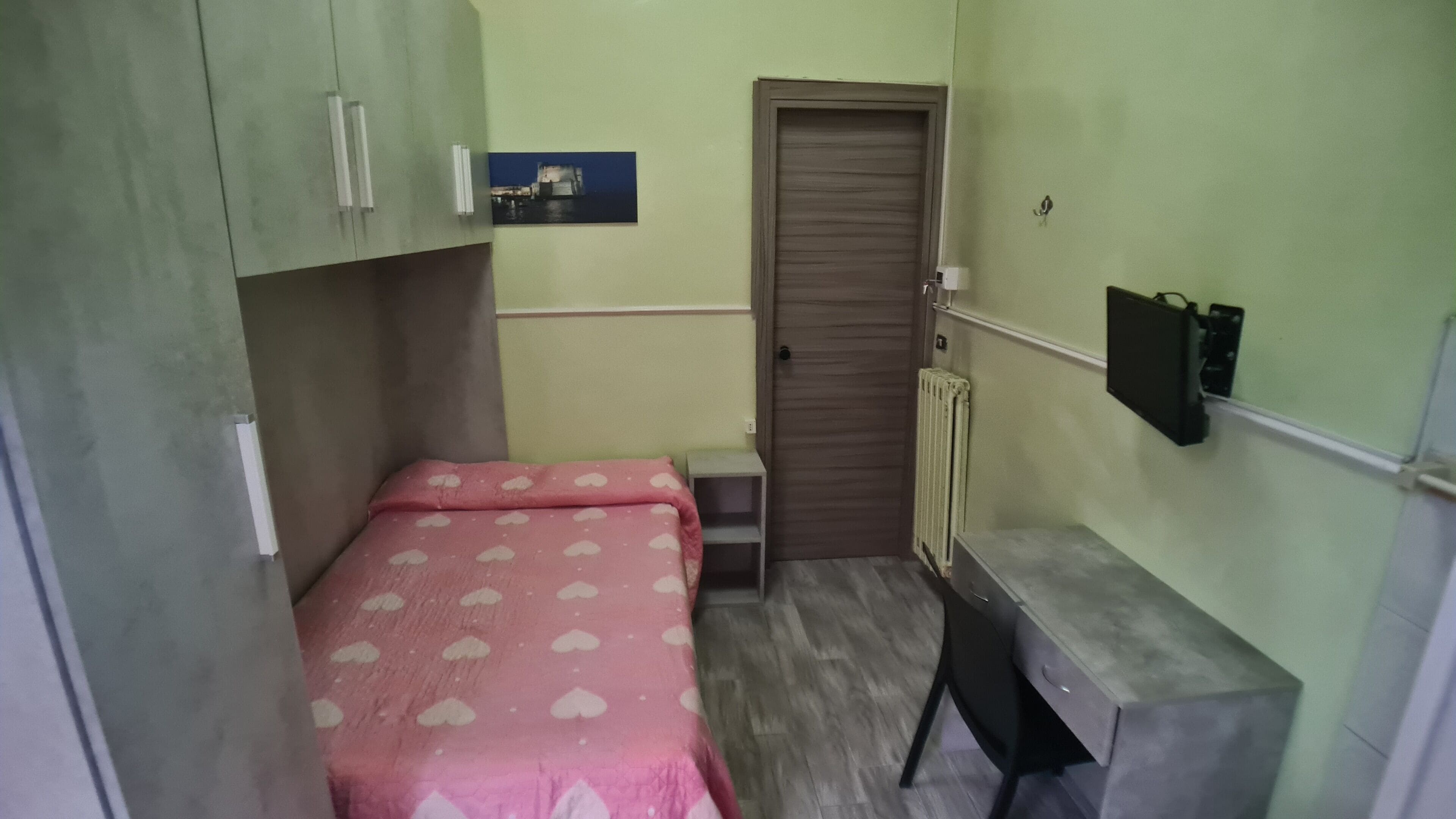 A small, compact room with a bed, a desk, and a wardrobe.