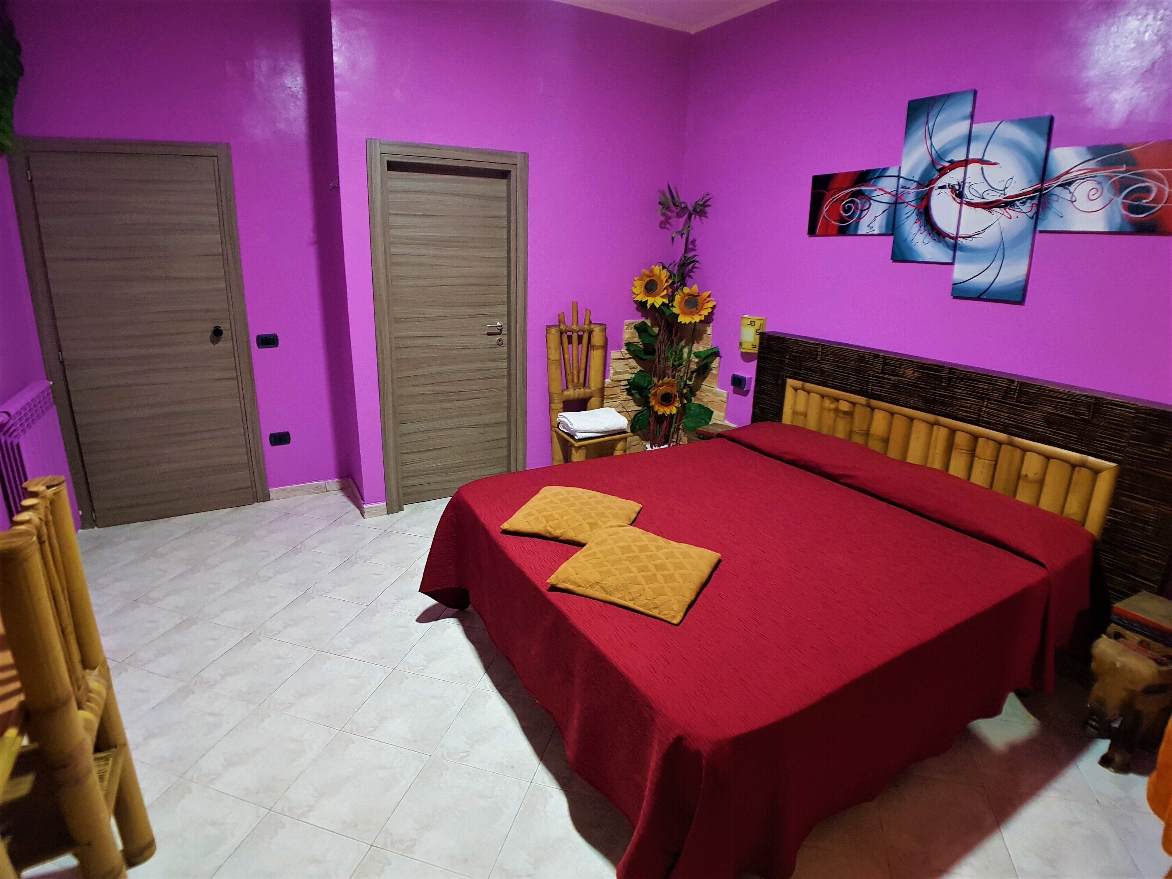 A room with a bed, a chair, a door, and a wall with a painting.