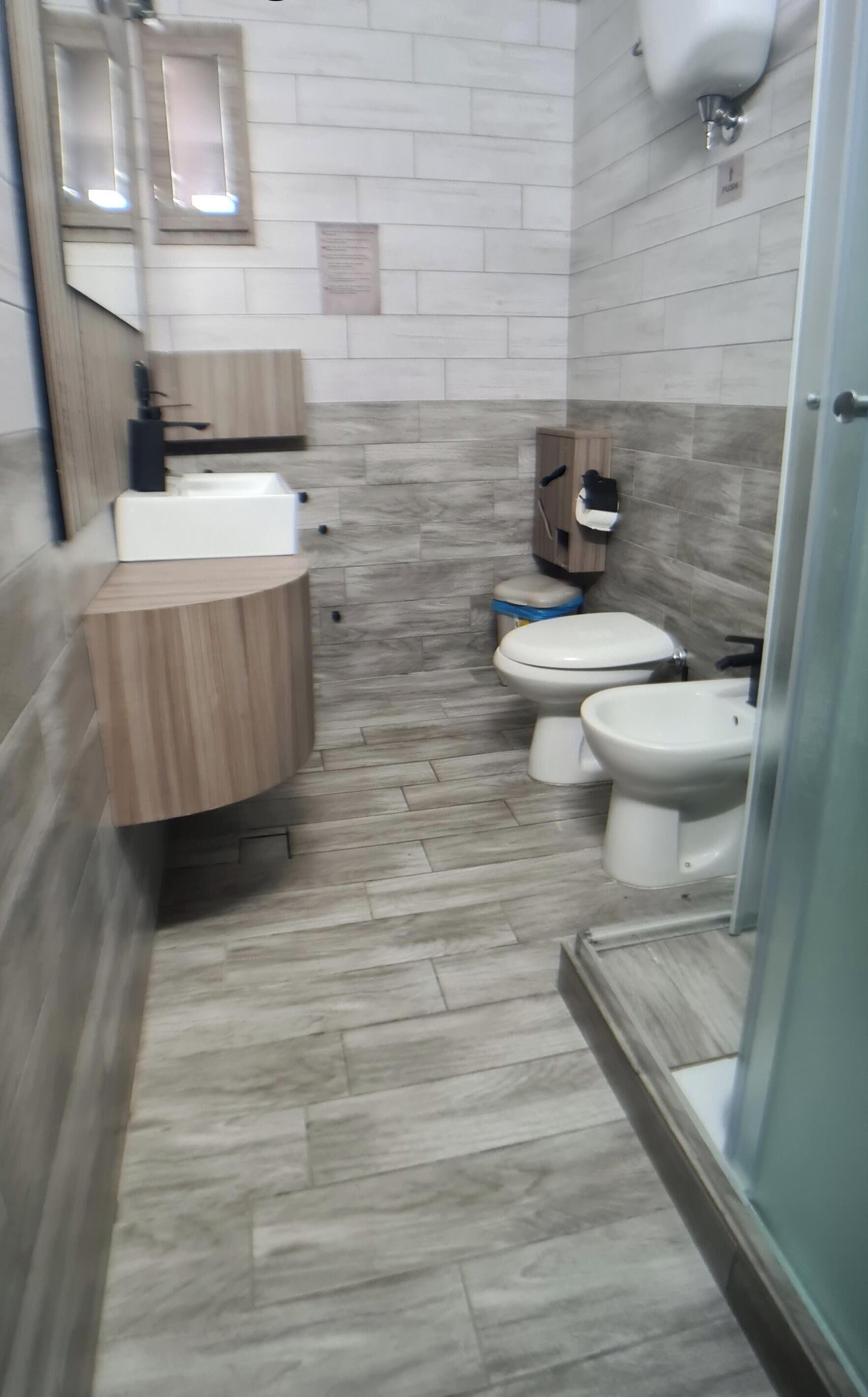 A bathroom with a wooden vanity, two toilets, a bidet, and a mirror.