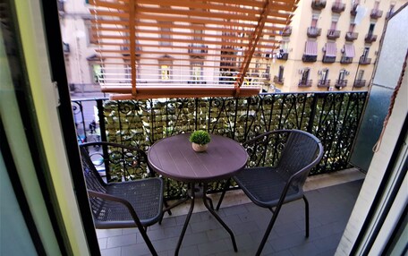 A balcony with a table and two chairs, a small potted plant, and a wooden pergola.