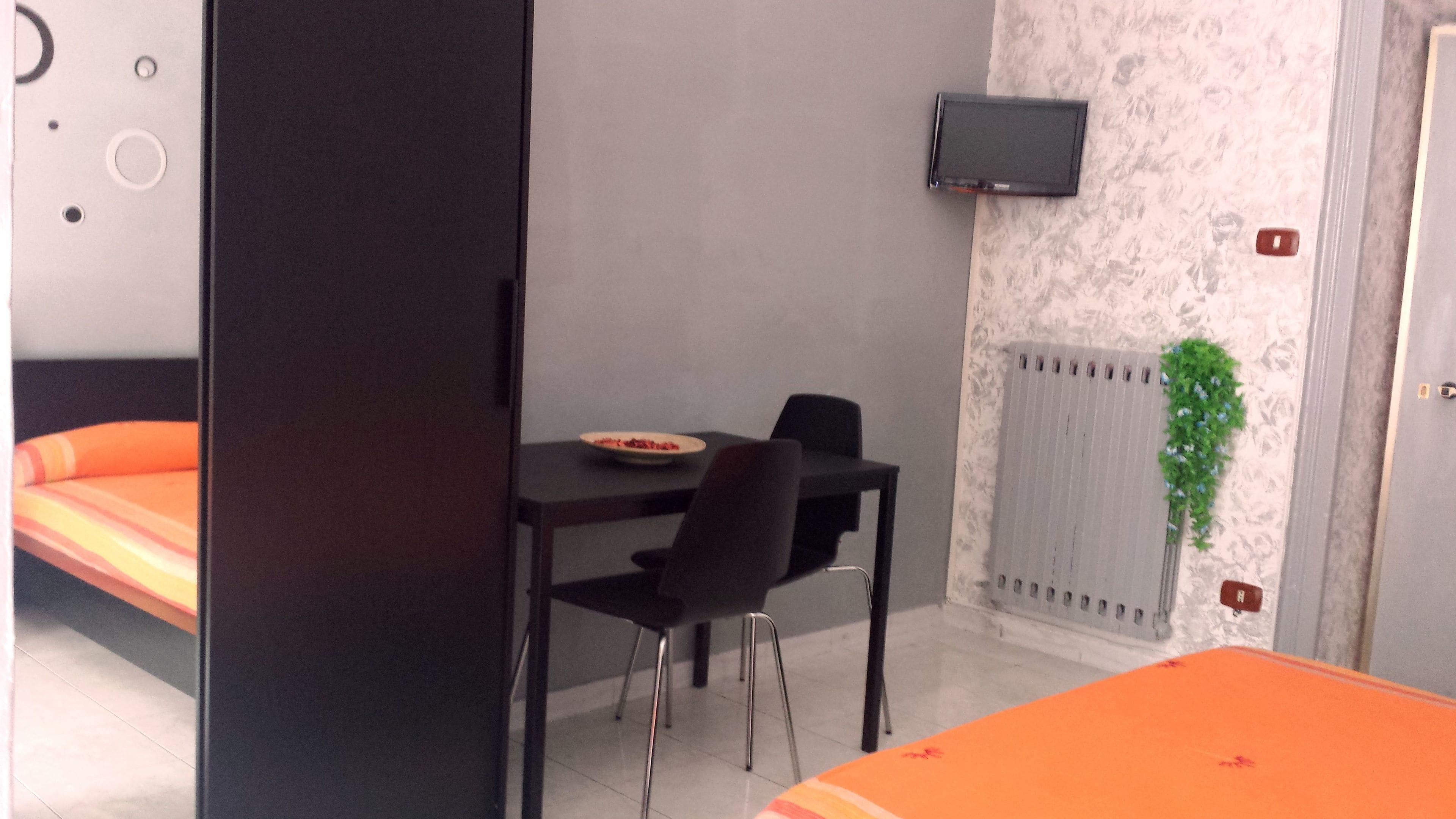 A room with a bed, a table with chairs, a TV mounted on the wall, and a radiator.