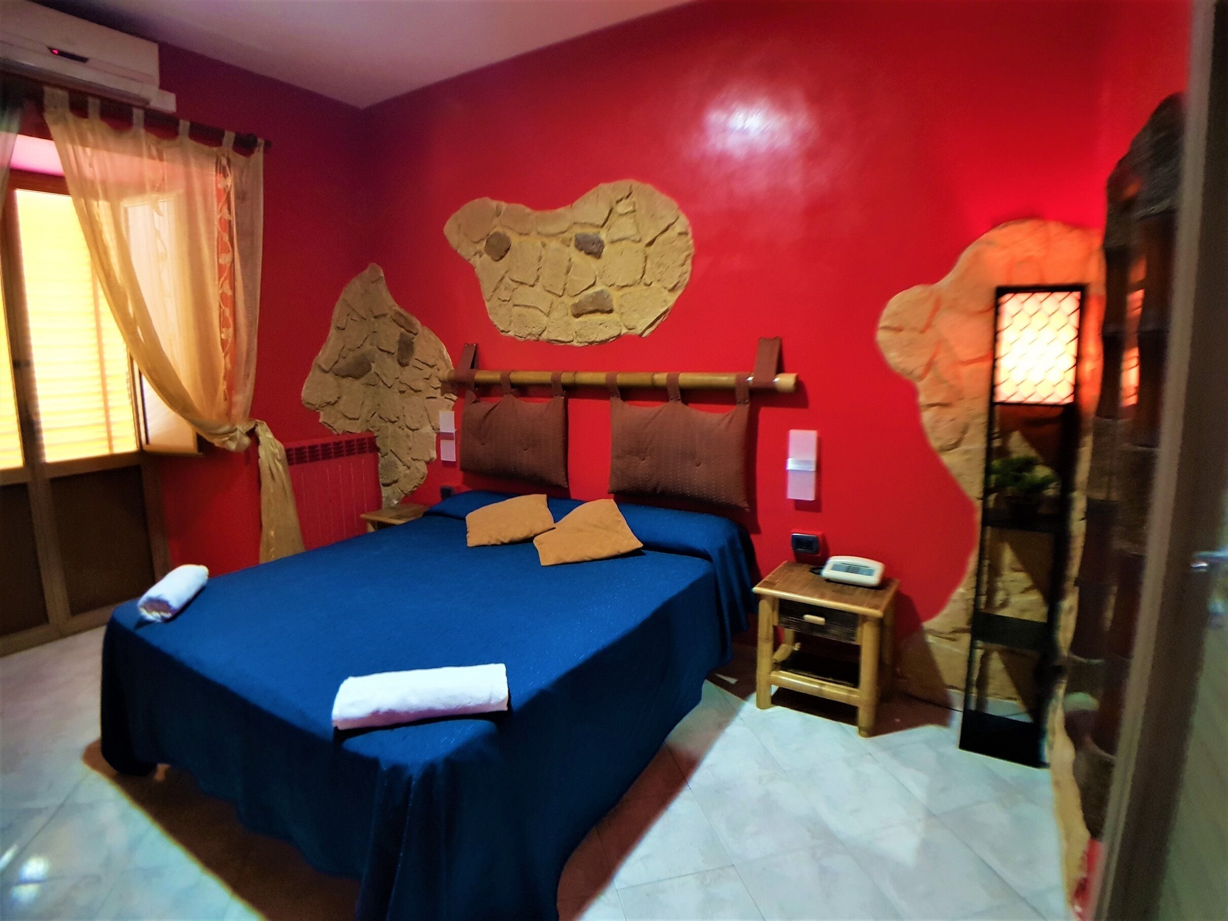 A room with a bed, a nightstand, a wall clock, and a window with curtains.