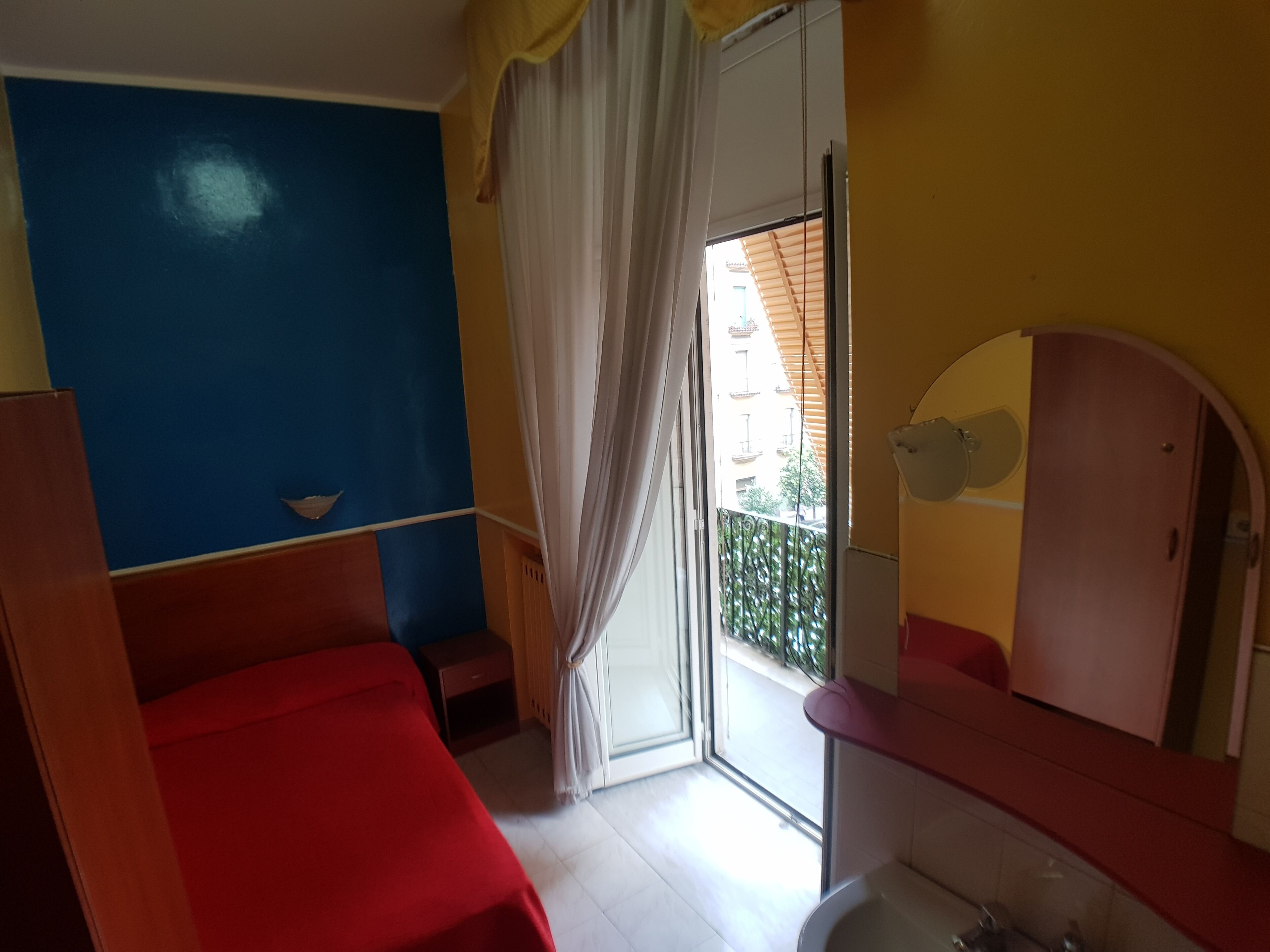 A room with a bed, a bathroom with a mirror and sink, and a sliding glass door leading to a balcony.