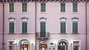 Un edificio con varias ventanas, contraventanas verdes y dos entradas iluminadas con letreros que indican 'Albergo Alla D'oro'.