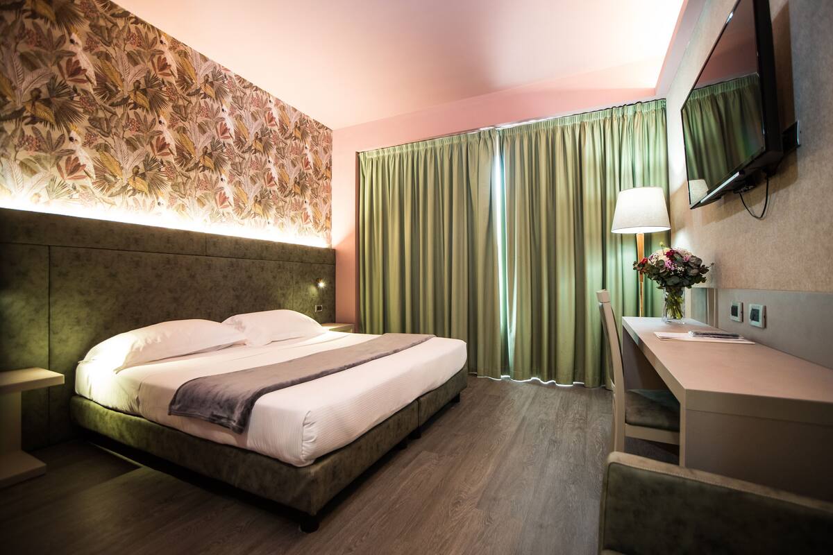 A hotel room with a bed, a desk, a lamp, and a mirror.