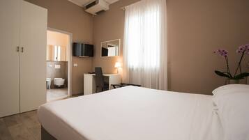 Une chambre d’hôtel comprenant un lit, un bureau, une chaise, une télévision, un miroir et une salle de bain visible à travers une porte ouverte.
