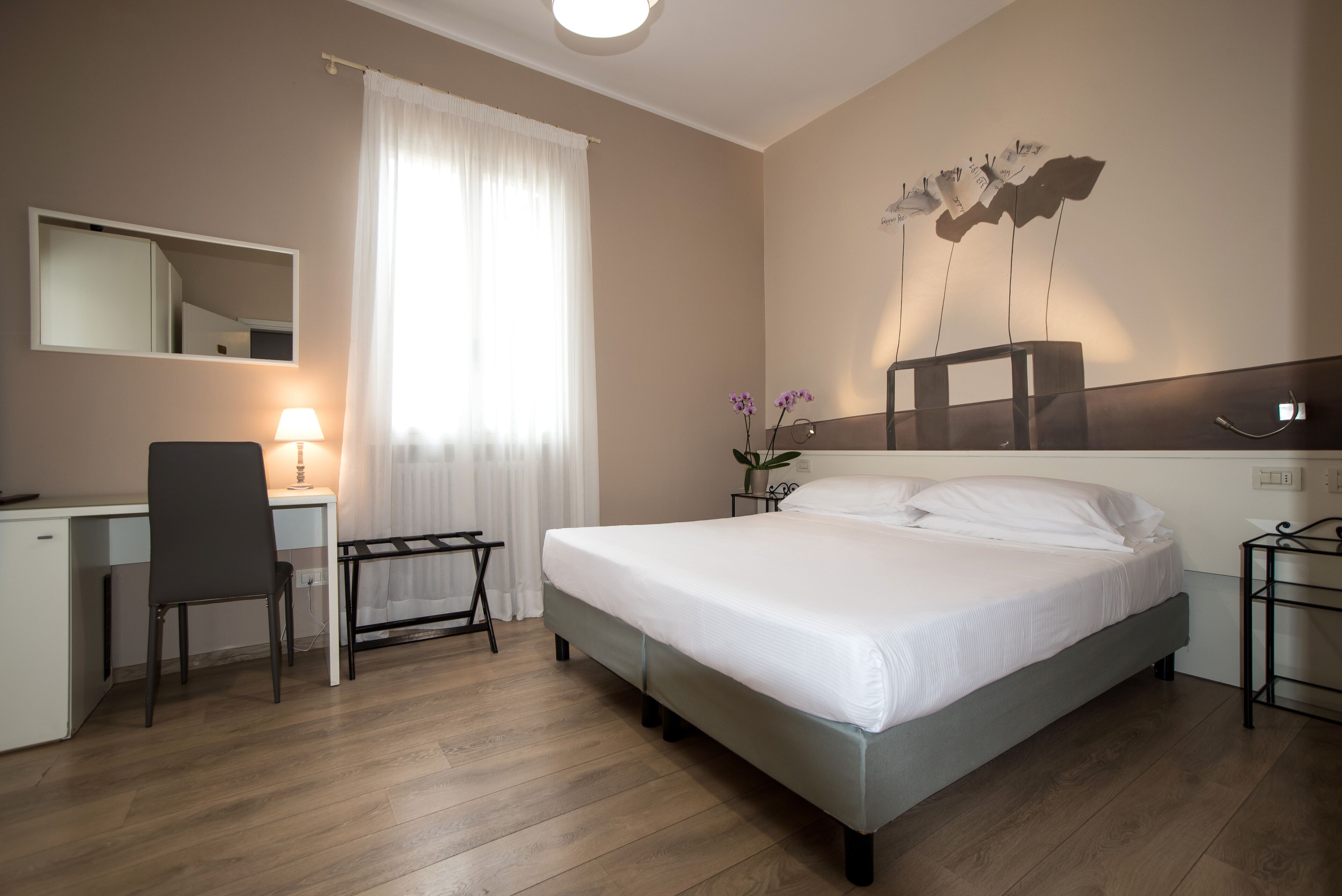 Habitación de hotel con cama, escritorio, silla y lámpara de pared.