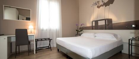 Habitación de hotel con cama, escritorio, silla y lámpara de pared.