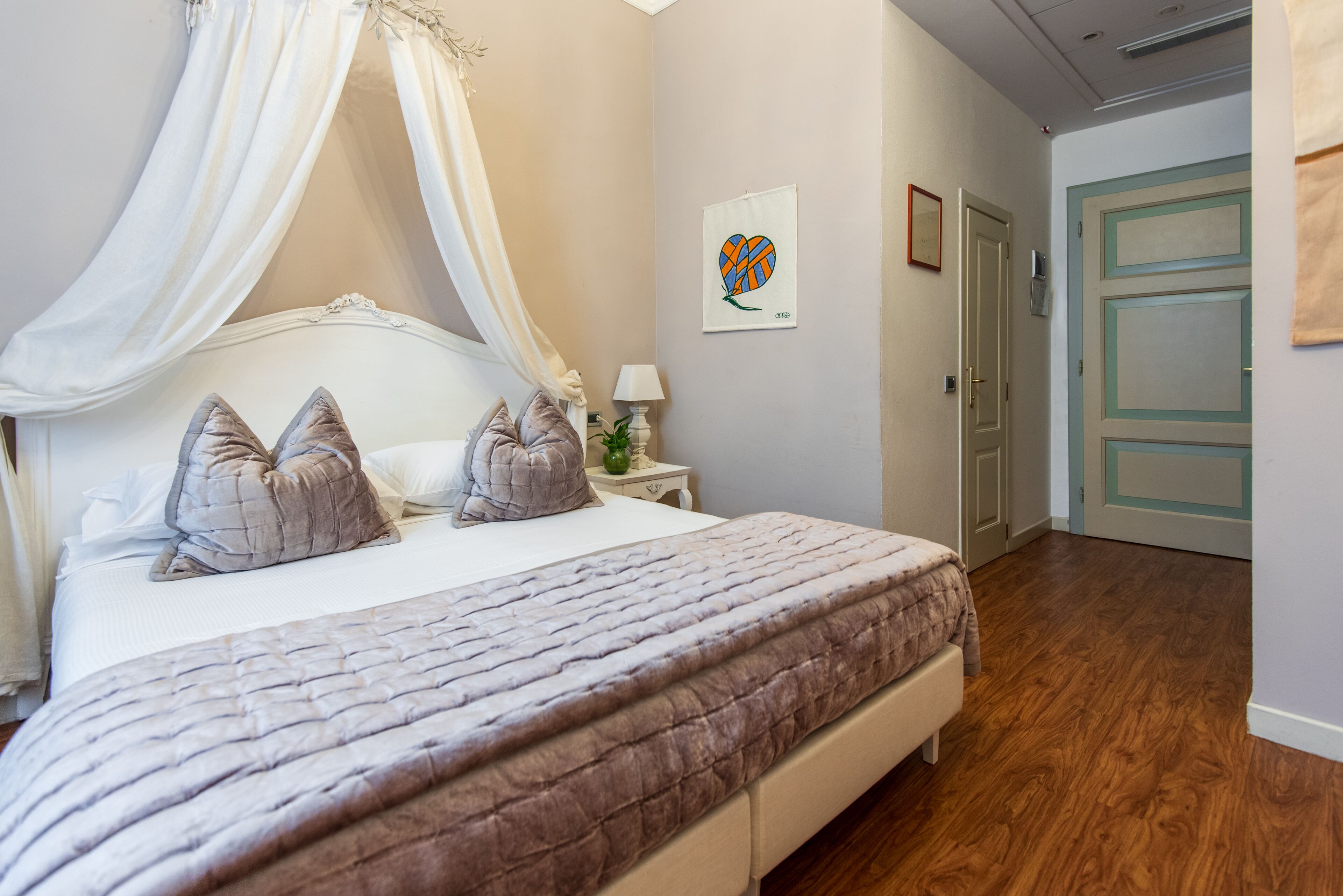 A bedroom with a canopy bed, a bedside table with a lamp, and a wall art piece.