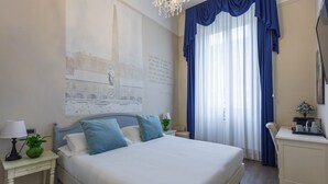 Un dormitorio ordenado con cama, mesitas de noche, un escritorio y un amplio ventanal con cortinas.