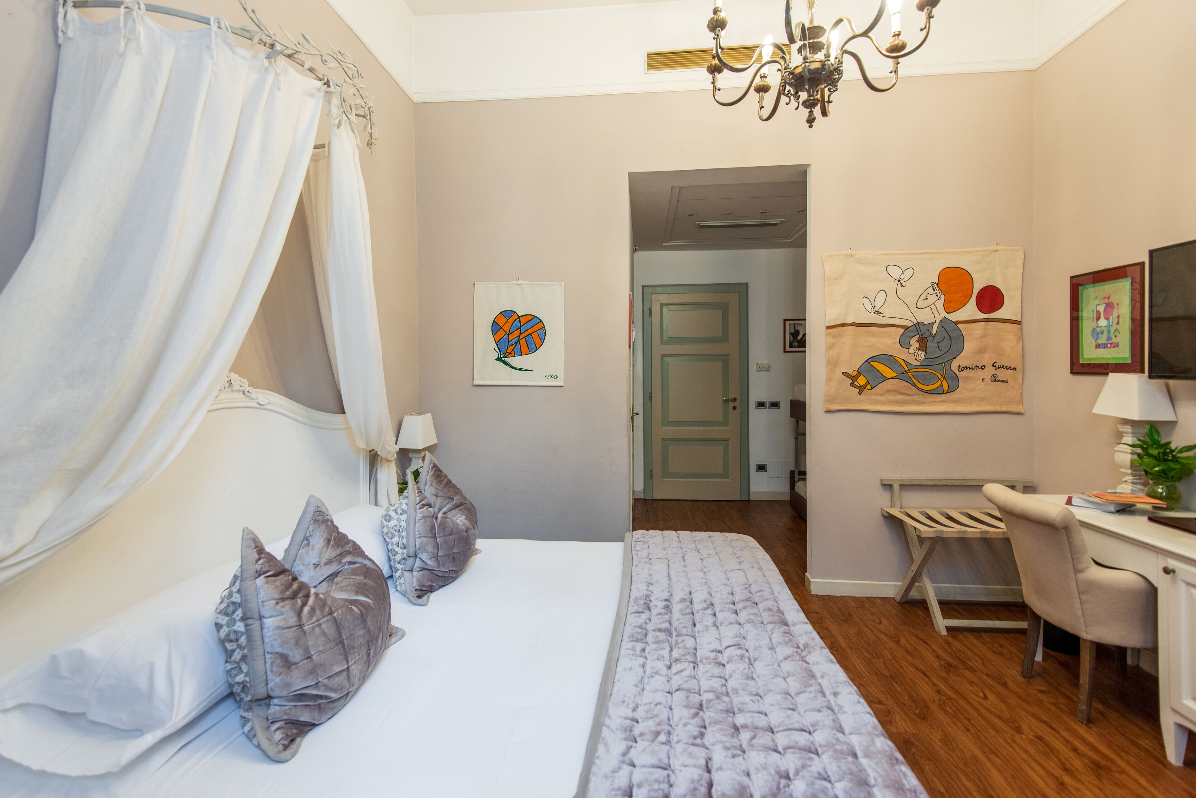 Un dormitorio con una cama, un escritorio y una silla. Hay dos almohadas en la cama, un dosel y una araña.