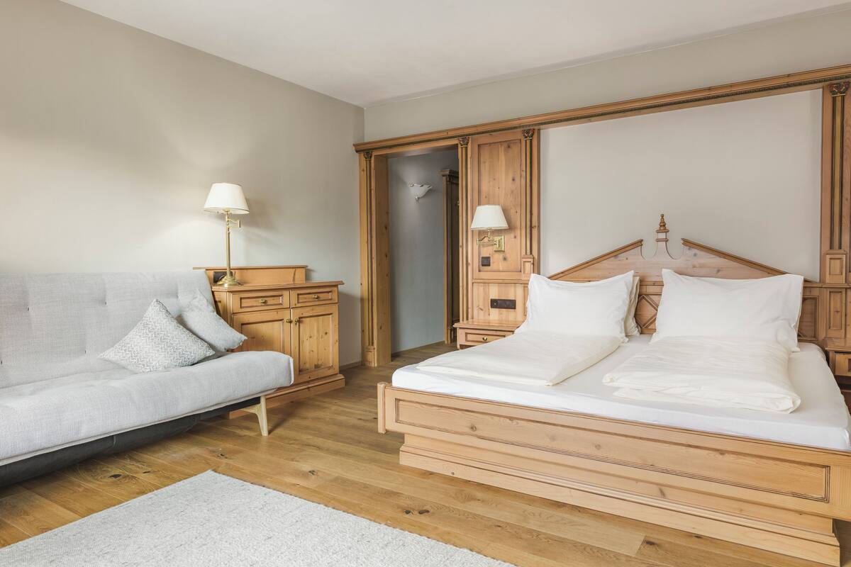 A bedroom with a bed, a sofa, wooden furniture, and a nightstand with lamps.