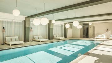 Une piscine avec des chaises longues et un plafond orné de luminaires suspendus.