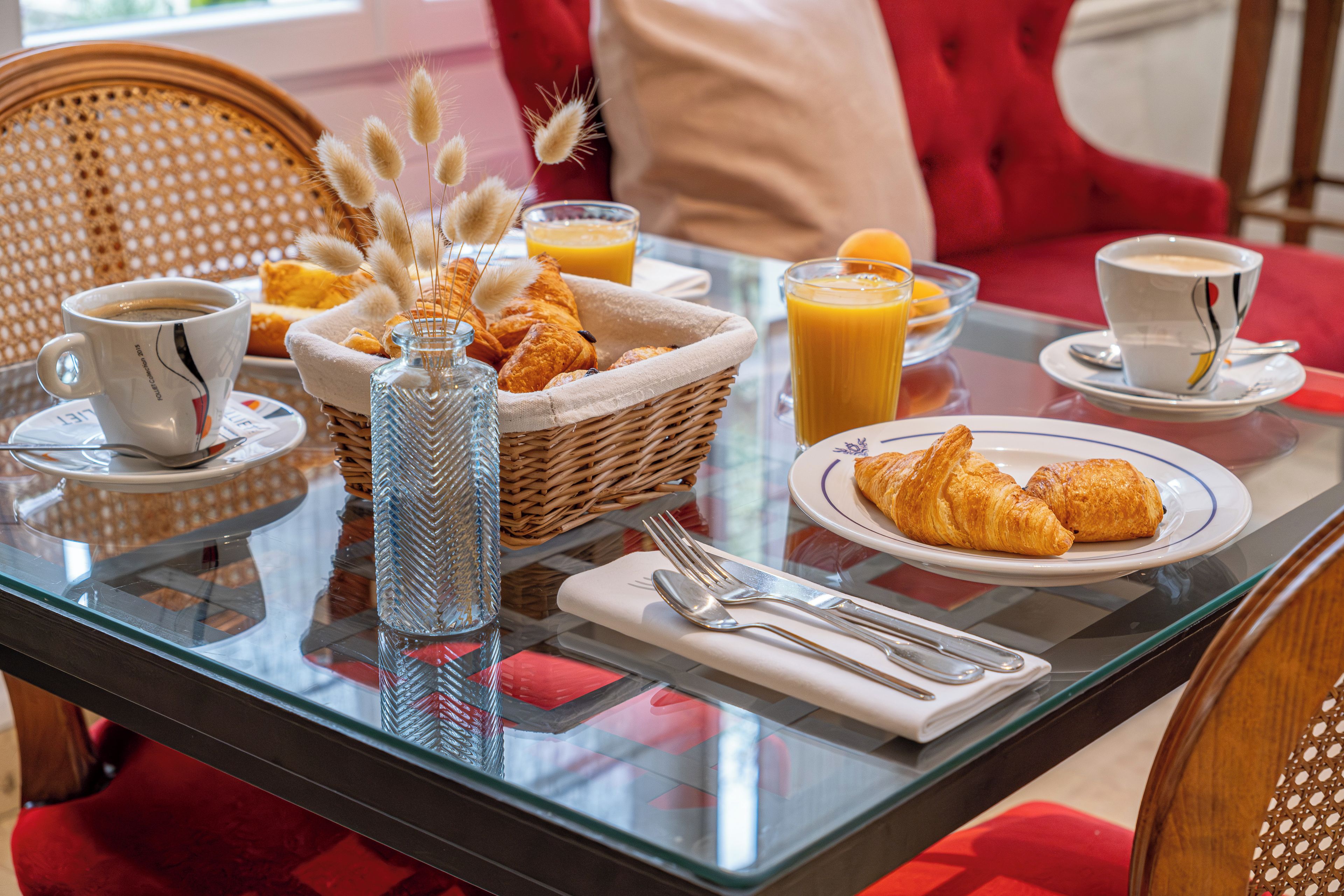 A breakfast setting with croissants, juice, coffee, and a decorative vase on a glass table.