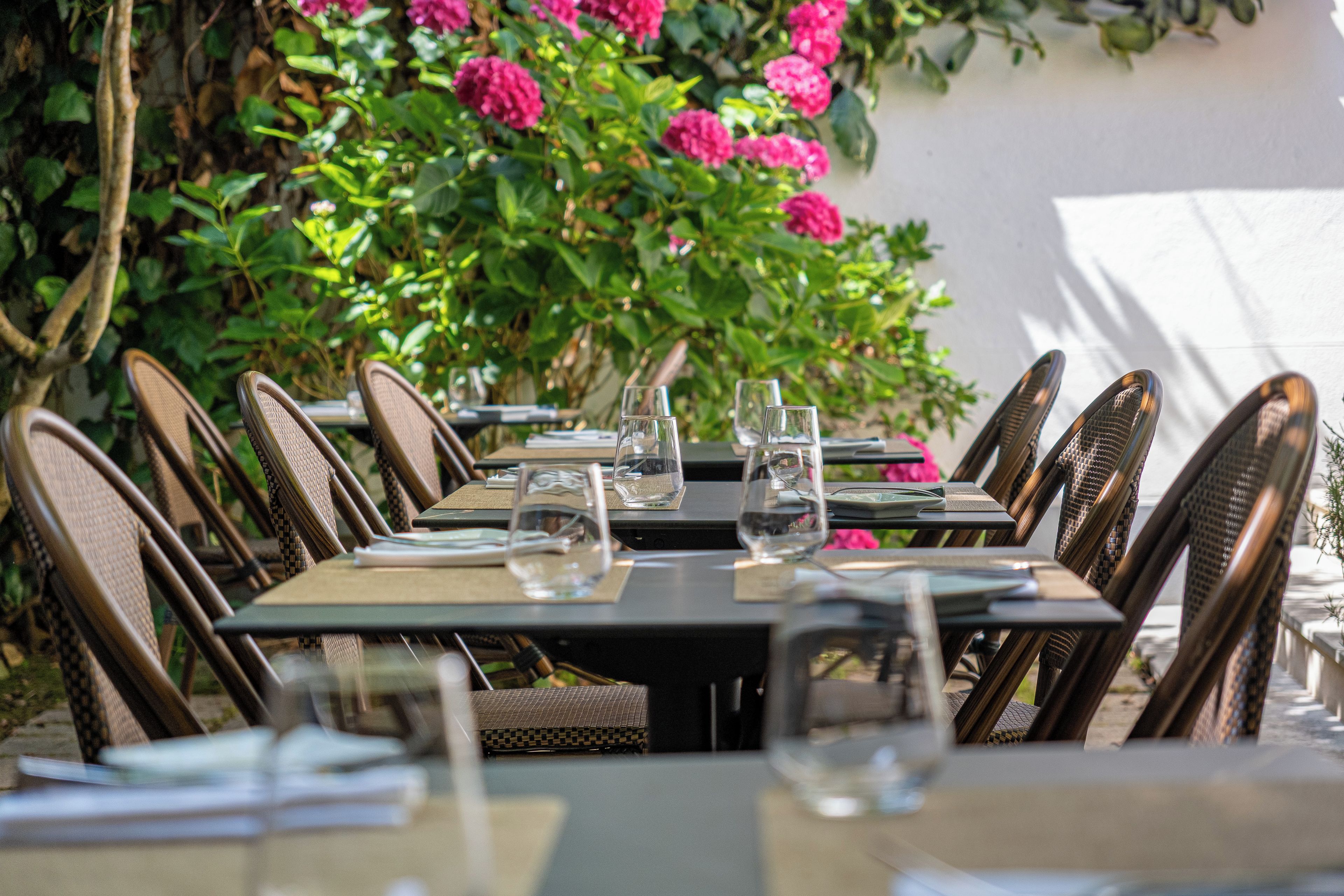 Un espace de restauration en plein air, avec des chaises et des tables en osier, entouré de verdure et de fleurs.