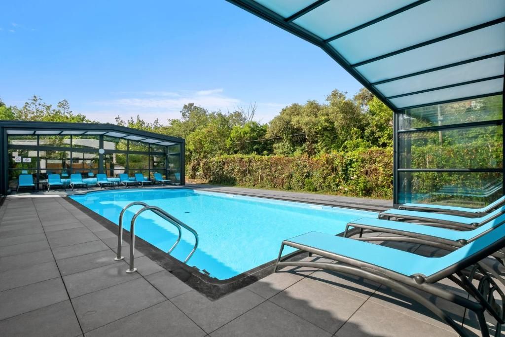 Una piscina con lettini e un'area vetrata, immersa nel verde.
