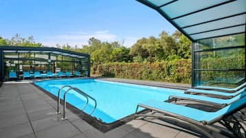 A swimming pool with lounge chairs and a glass-enclosed area, surrounded by greenery.