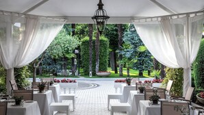 Un espace de restauration en plein air avec des tables et des chaises blanches, entouré d’une végétation luxuriante et bordé d’un chemin pavé.