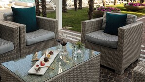 Un coin salon aménagé avec des meubles en osier, comprenant une table en verre, deux chaises et une vue sur une piscine et des palmiers.