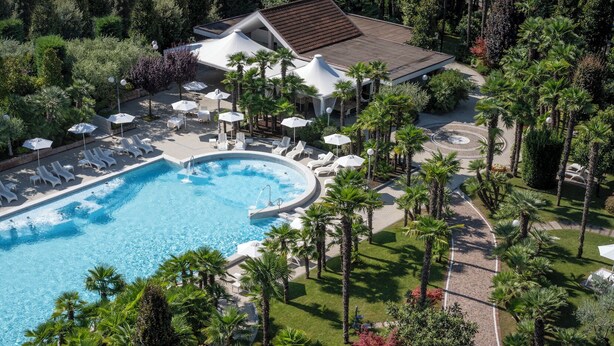 Vue aérienne d’un complexe hôtelier avec une piscine, des chaises longues et des palmiers.