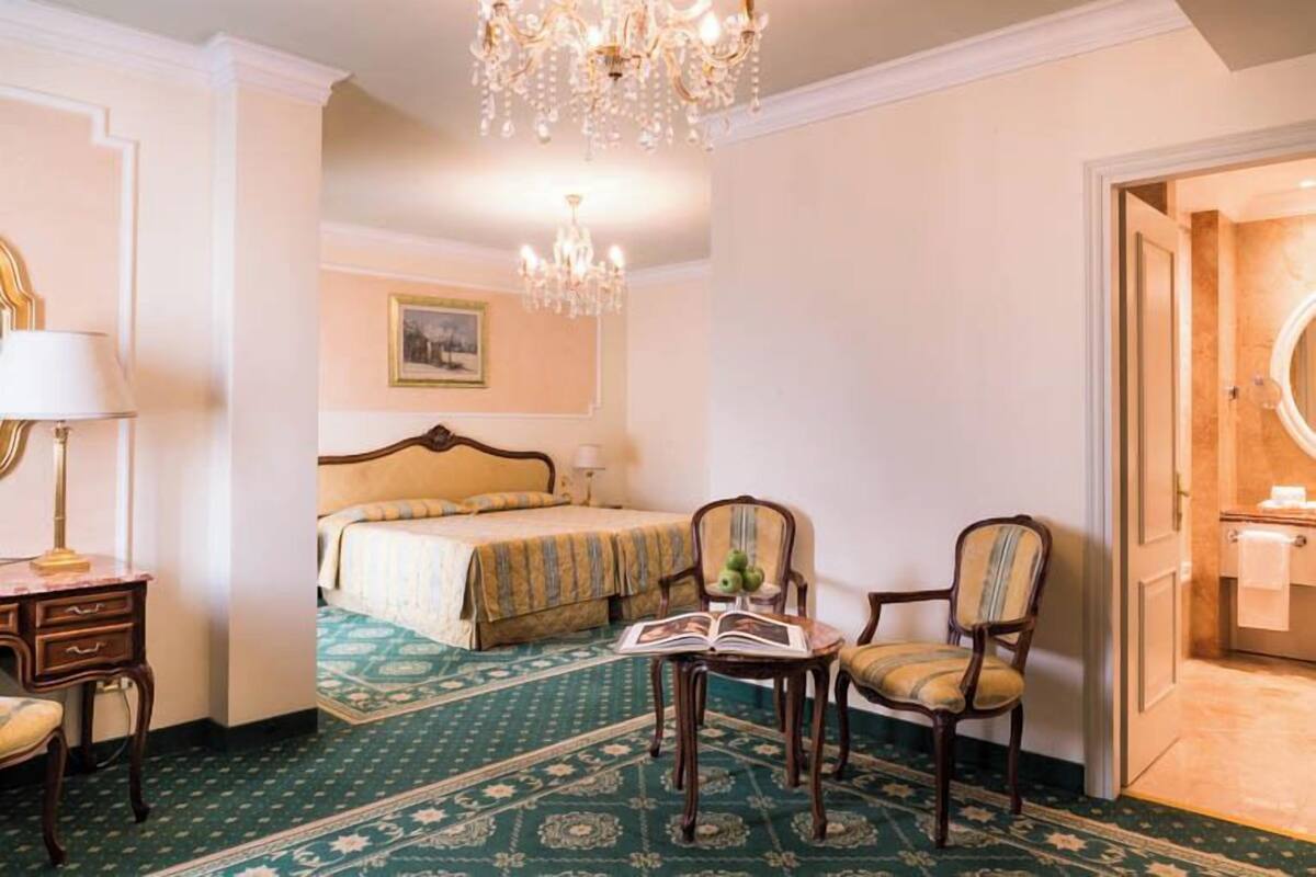 Ein Hotelzimmer mit Bett, Schreibtisch, Stuhl, einer Kandelaber und einem durch eine offene Tür einsehbaren Badezimmer.