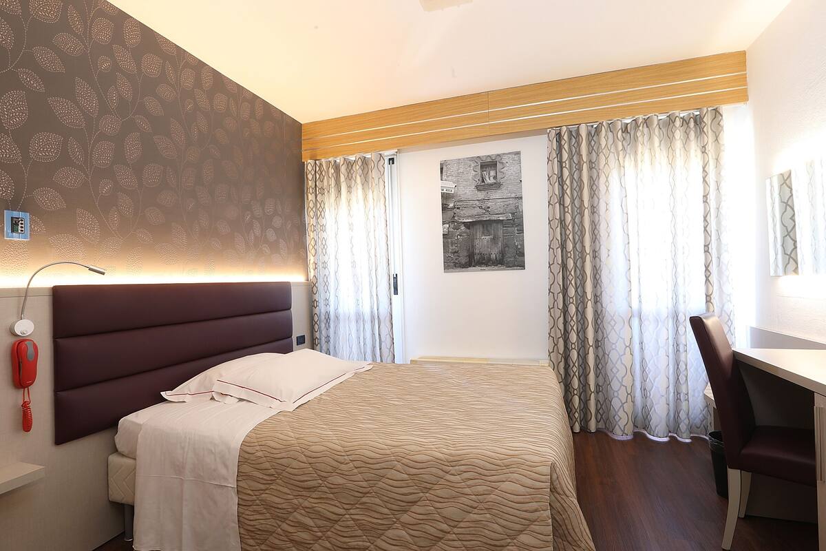 Habitación de hotel con cama, escritorio, silla, teléfono y lámpara en la pared.