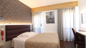 Une chambre d’hôtel équipée d’un lit, d’un bureau, d’une chaise, d’un téléphone et d’une lampe fixée au mur.