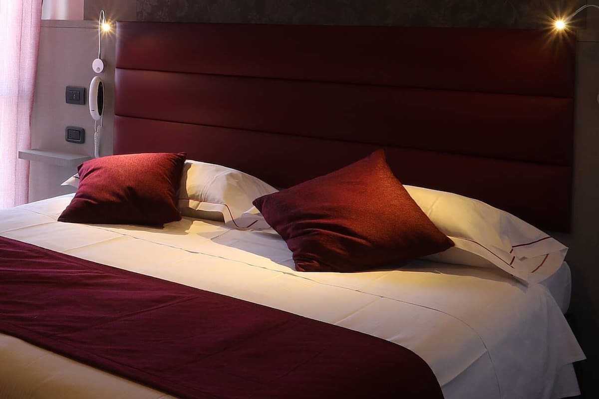 Una cama con cabecera roja, ropa de cama blanca y dos almohadas rojas.