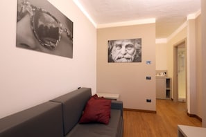 Una habitación moderna con un sofá gris, una almohada roja, un cuadro de un rostro en la pared y una mesita.
